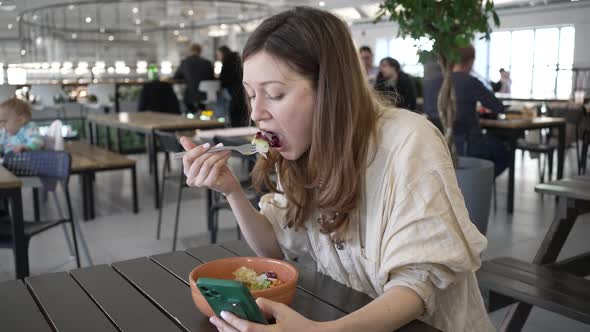 Woman in Cafe Eats Salad Scrolling Social Media Pages