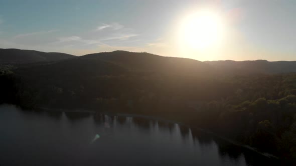 Slow aerial flight over a canadian lake in quebec which is surrounded by trees at sunrise with the s