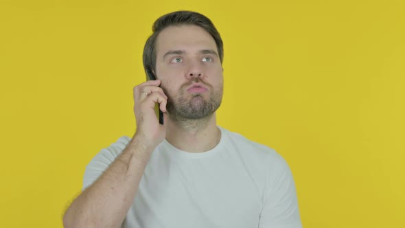 Young Man Talking Angry on Phone on Yellow Background