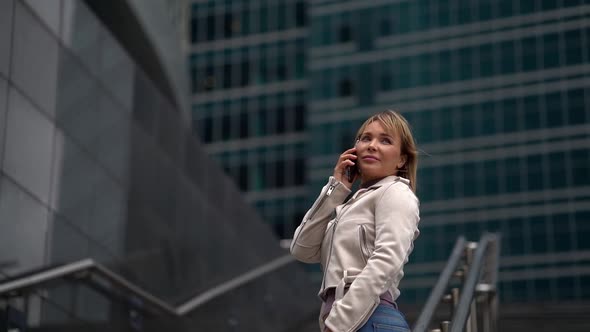 Business Woman Blonde Talking on the Phone Standing on the Stairs in the Background of a Beautiful