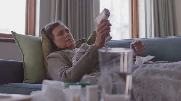 Woman measuring her temperature while laying on the couch at home