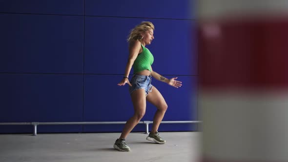 Slow motion shot of dancing blond woman in front of blue wall