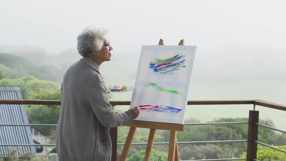 African american senior woman painting on canvas in the balcony at home
