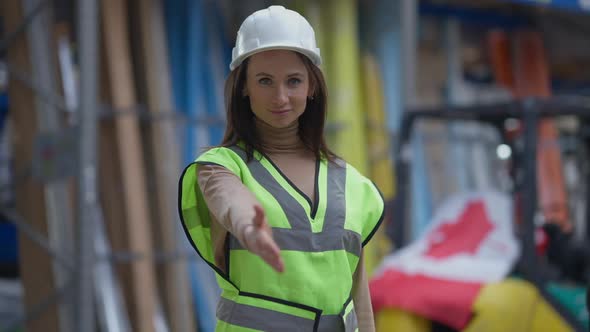 Smiling Slim Beautiful Caucasian Woman in Hard Hat Stretching Hand for Greeting Looking at Camera