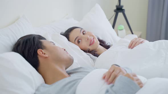 Asian attractive young couple lying down on bed to rest in bedroom.