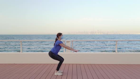  Girl in Medical Mask Does Squatting in Front of Sea