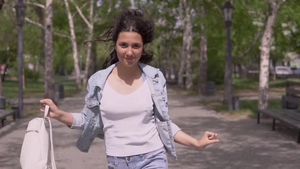 Funny Girl in a Good Mood with Long Hair with a Backpack in Hand Walks Down the Street in Sunny