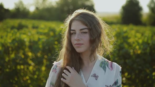 Portrait of Young Lady in Dress Looking at Camera Among Summer Green Field