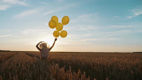 Woman with Balloons in Hand Runs Through a Wheat Field at Sunset