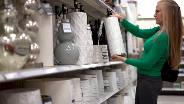 Low angle shot of pretty, blonde, mature woman looking at lamp shades and lamps in a store display.