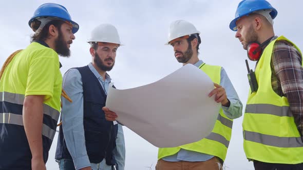 Group of Engineers and Workers Looking at a Blueprint s in a Windmill Park