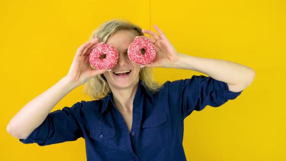 Crazy Cheerful Blonde Girl is Smiling Having Fun and Looking Through Two Red Donuts on Her Eyes
