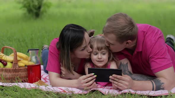 Family Weekend Picnic. Daughter Child Girl with Mother and Father Watching Online Movies on Tablet