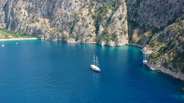 aerial drone circling a large sailboat anchored in the blue ocean of Butterfly Valley panning upward