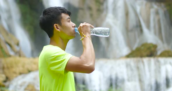 Man Drinking Water, Waterfall at Background