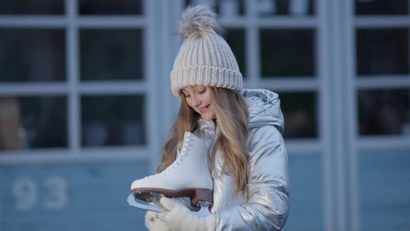 Happy Cute Caucasian Girl Holding Ice Skates Looking at Camera and Smiling