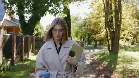 Young Girl Walks in the Green Neighborhood on a Sunny Autumn Day Wearing a Coat