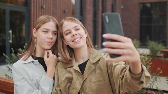 Cheerful Twin Sisters Taking Selfie Outside
