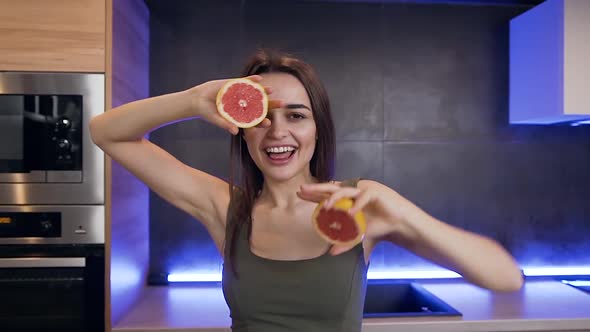 Young Brunette which Holding Two Halves of Grapefruit on the Kitchen Background