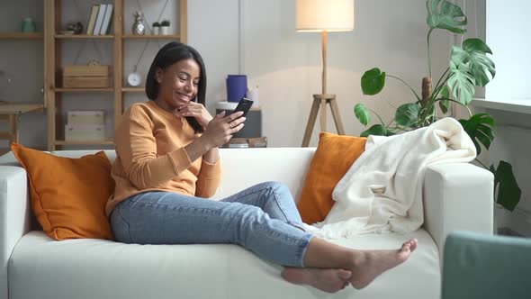 Woman Using Phone and Smiling Sitting on Couch in Light Room Spbd