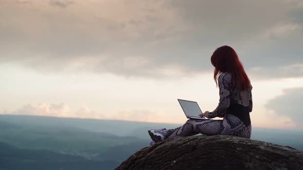 Girl Blogger Traveler is Typing Text on Laptop While Sitting on Top Mountain