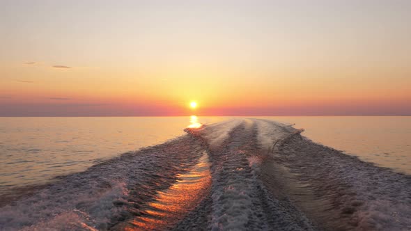 Fast boat rush on flat water, look back to bright sunset and clear sky