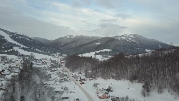 Flight Over a Village in Carpathian Mountains and a Ski Resort Next To It. Bird's Eye View of Snow