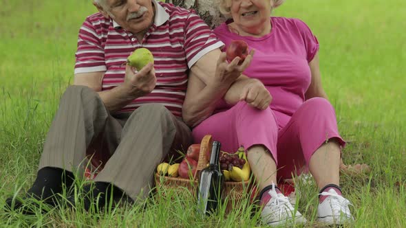 Family Weekend Picnic in Park. Active Senior Old Caucasian Couple Sit on Blanket and Eating Fruits