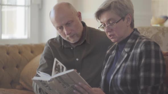 Elder Couple, Man and Woman, Sitting on the Sofa with a Book and Talking and Smiling To Each Other