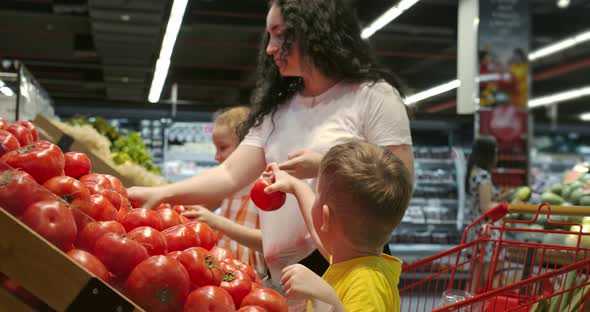 Cute Woman with Little Happy Son and Daughter are Choosing Fresh Vegetables Together at the Grocery