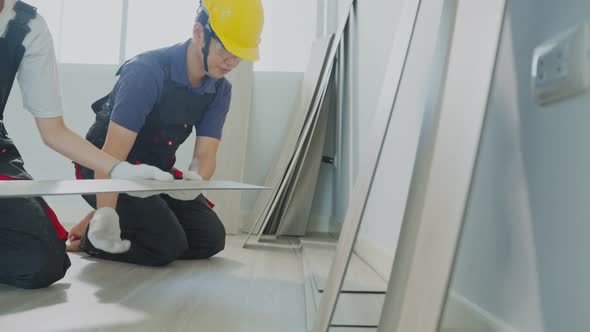 Slow motion of construction builder worker wear hardhat installs laminate board on floor at home.