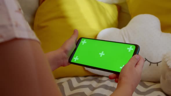 Preschool Girl Holds a Smartphone with a Green Screen in Her Hand