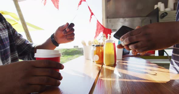 Midsection of african american man paying male owner for coffee by credit card at food truck