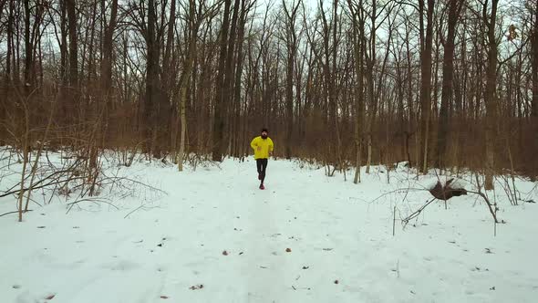 Young Bearded Man in Yellow Coat Running in Forest on Cold Winter Day