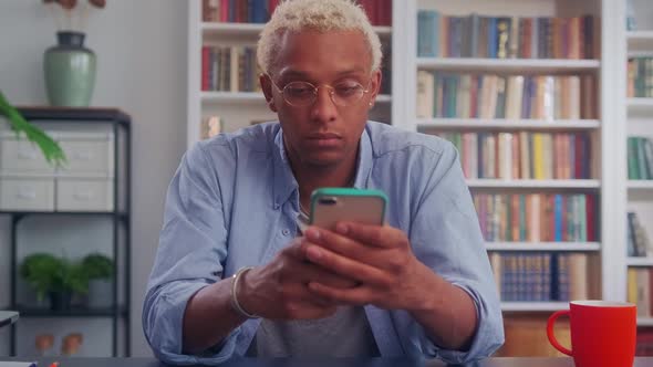 Young African American Man Holding Phone in Hands and Typing Something