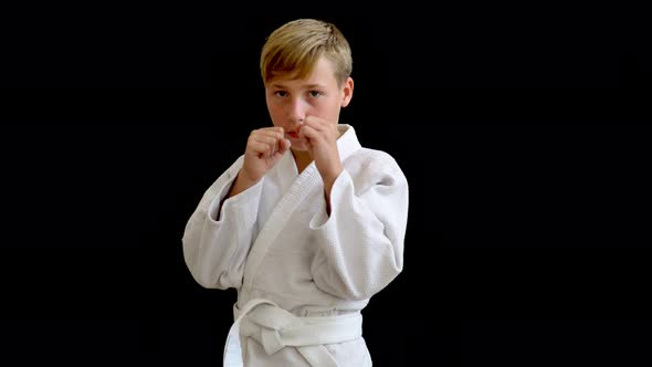 A Young Athlete in a White Kimono Stands on a Dark Background. The Boy Has Blond Hair and a European