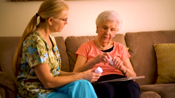 Closeup of home healthcare nurse going over medications with elderly woman while sitting in living r