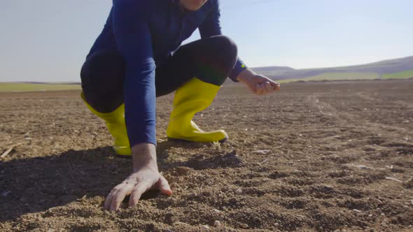 The farmer is covering the seeds with soil with his hand.