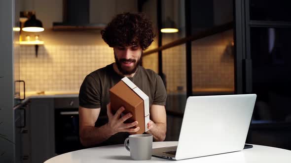 Happy Surprised Beared Young Man Opening Gift Box with Present During Video Call on Laptop Computer