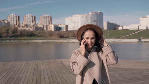 Business Lady in a Coat and Hat Talking on a Mobile Phone on the Street