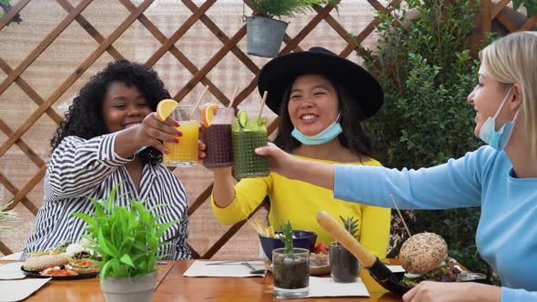 Multiracial friends toasting with fruits fresh smoothies in coffee brunch bar