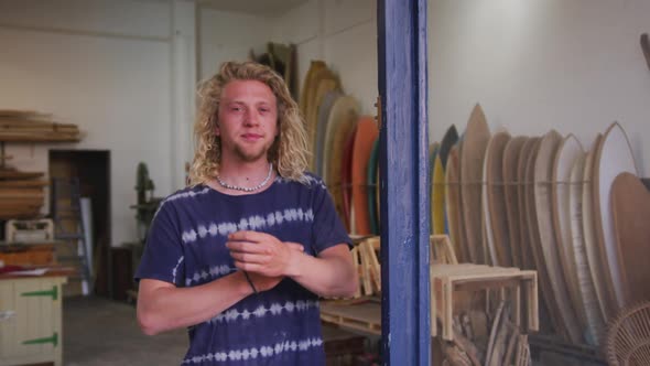 Caucasian male surfboard maker leaning on a door frame of the entrance with his arms crossed