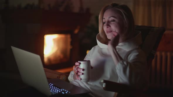 A Young Woman Having Video Call on a Laptop Near a Fireplace