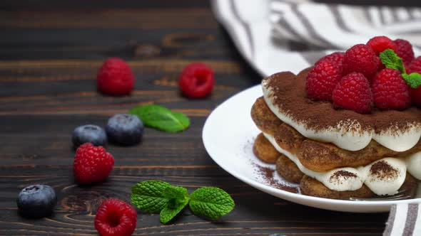 Portion of Classic Tiramisu Dessert with Raspberries and Blueberries on Wooden Background