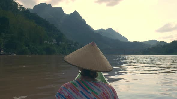 Woman with traditional hat cruising on the brown water of the Nam Ou river Laos