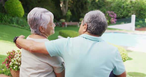 Video of back view of biracial senior couple embracing in garden