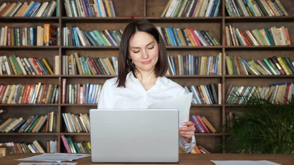 Young Woman Works with Papers By Laptop at Table in Library