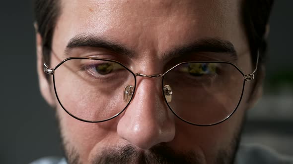 Portrait of serious young man looking at display wearing glasses at home