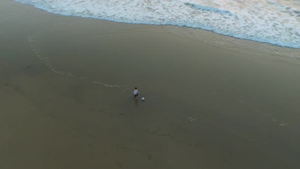 Aerial shot of little boy playing soccer on the beach at sunset.