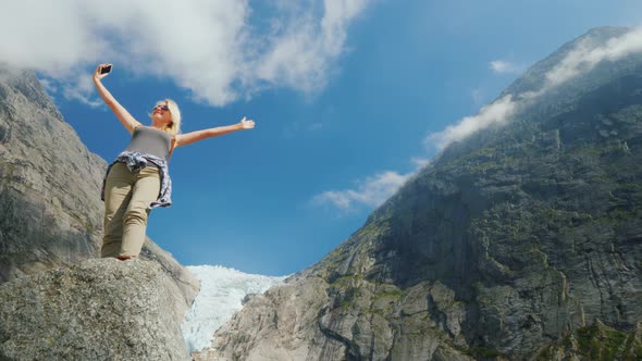 A Successful Young Woman Photographes Herself Against the Backdrop of Mountains and a Glacier in